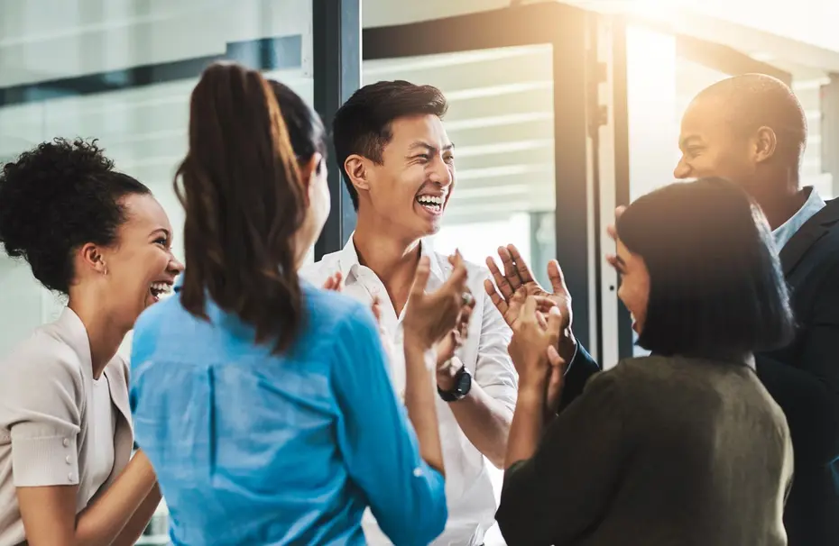 Un gruppo di cinque persone sta ridendo e applaudendo in un ambiente luminoso e professionale. I membri del gruppo sembrano godere di un momento di celebrazione o successo, con espressioni di gioia e entusiasmo.